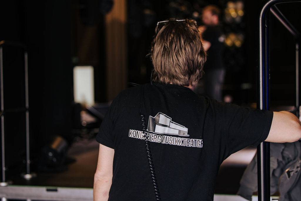 Ryggen til en tekniker med logoen til Kongsberg Musikkteater på ryggen