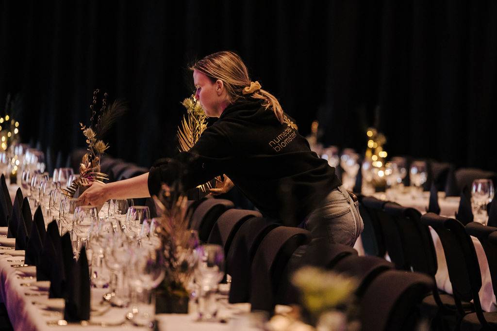 En dame som pynter et dekt bord med blomsteroppsatser
