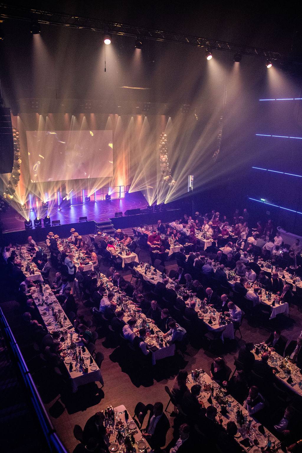 En fullsatt middagssal med lyssatt scene i lilla og gull