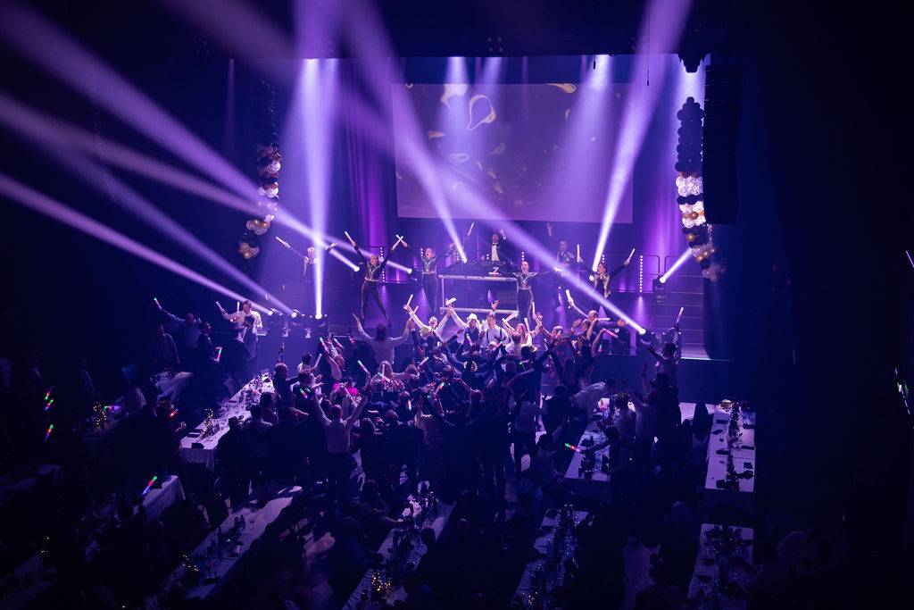 En event-sal i lilla lys med folk i salen flokket rundt scenen og god stemningh